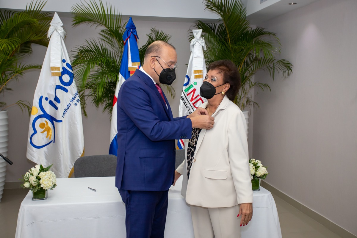 Ulises Rodríguez coloca el pin institucional de Proindustria a la directora del Inaipi, Besaida Santana. 