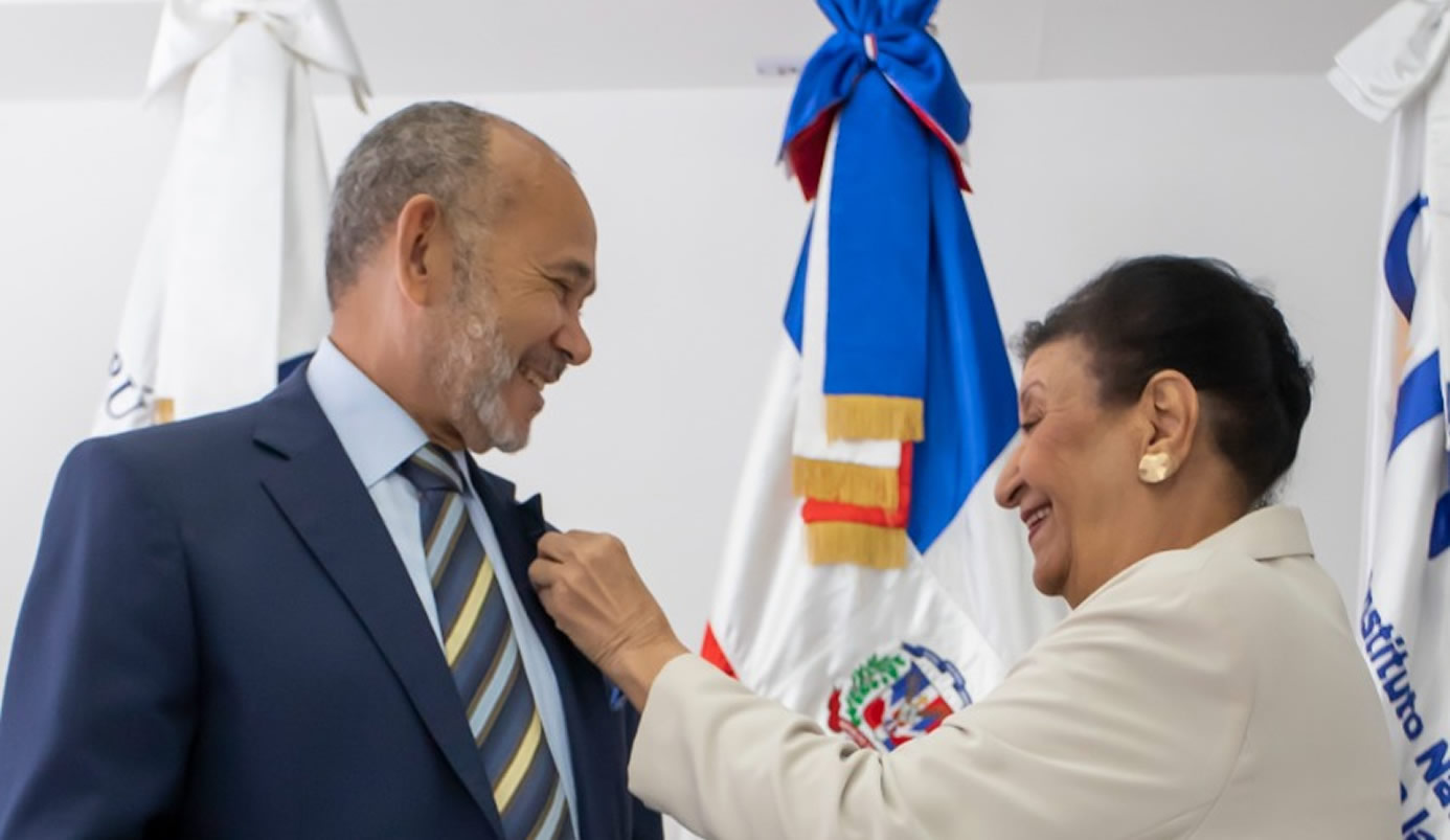 Besaida Manola Santana de Báez, directora ejecutiva del Inaipi coloca pin institucional a Víctor Castro, director ejecutivo del INABIE