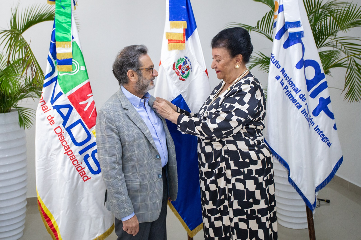 Besaida Santana, directora ejecutiva del INAIPI coloca pin institucional a Carlos José Yunén Bojos, presidente del CONADIS